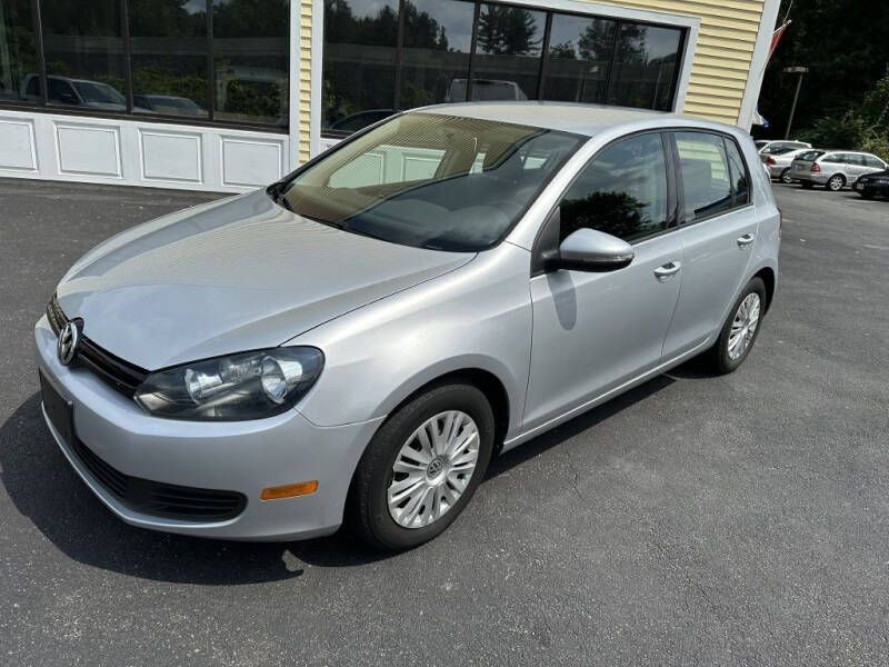 Silver hatchback car parked in front of a building with large windows and a yellow siding facade.