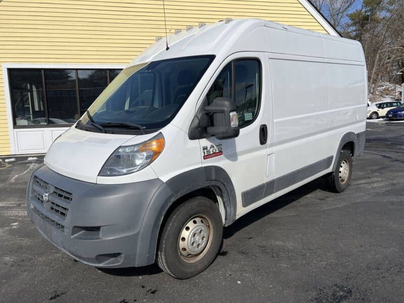 White cargo van parked on a paved area by a yellow building with large windows.