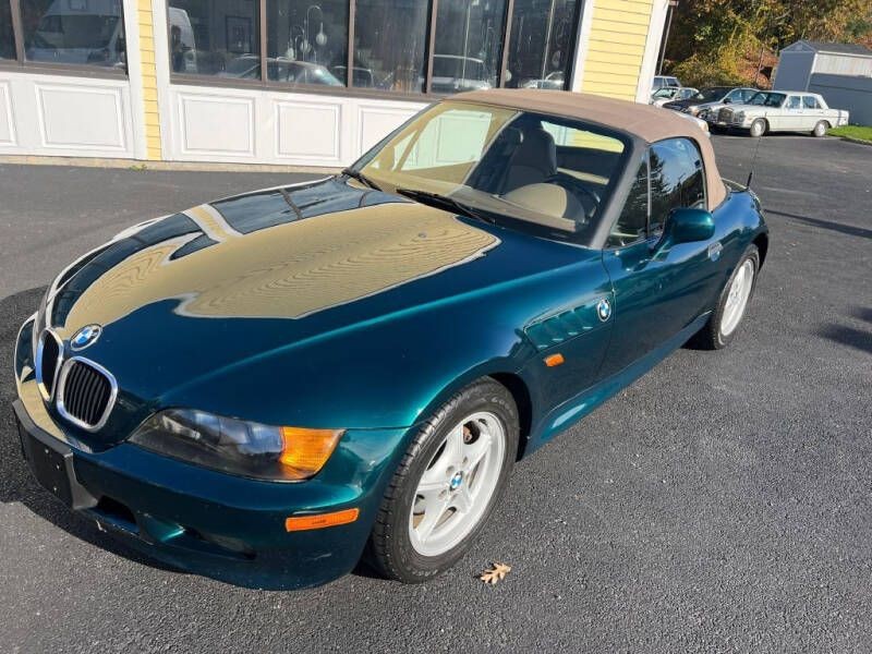 Green convertible sports car with a beige soft top parked on a driveway, reflecting yellow building walls.